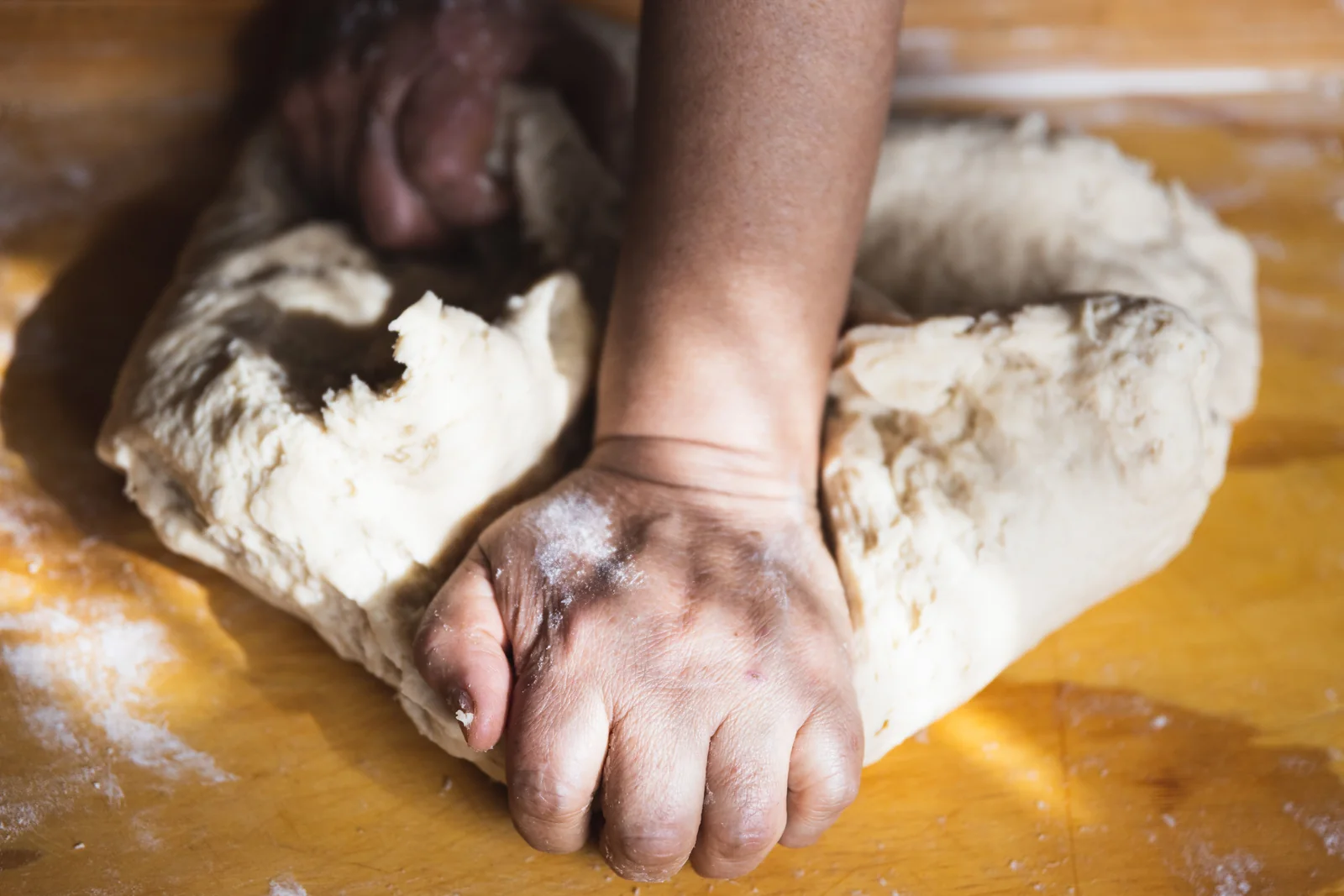 Hands kneading dough on a floured wooden surface