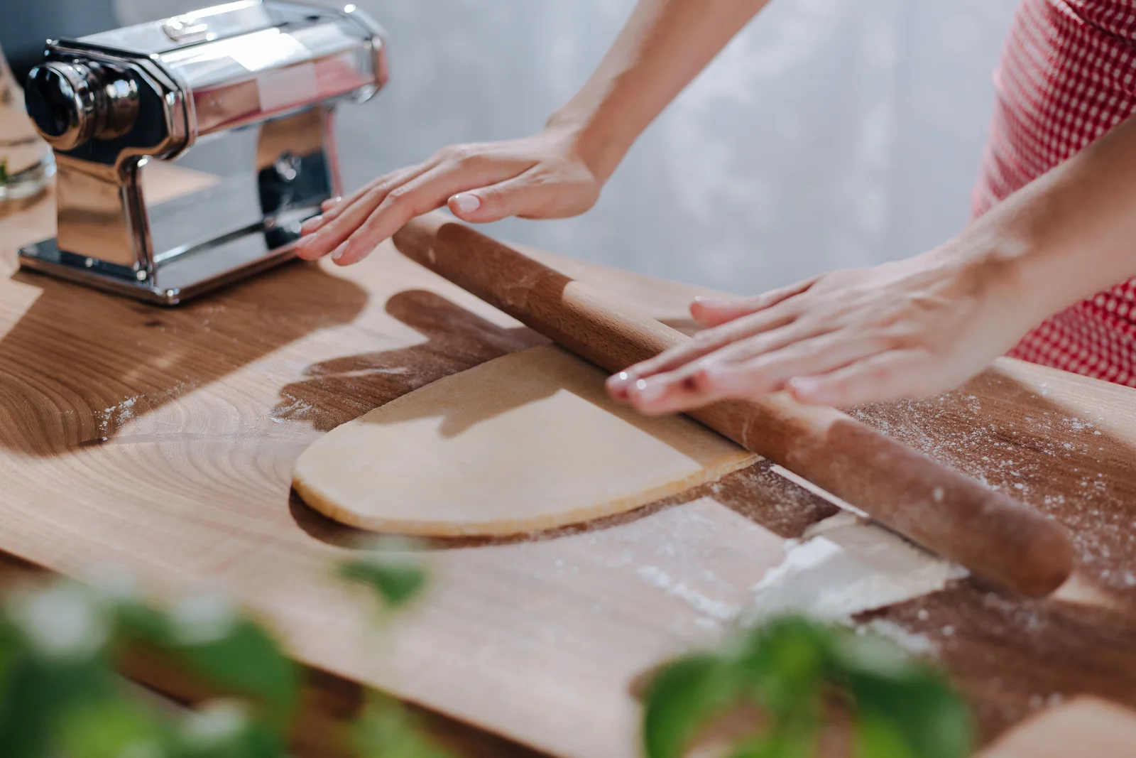 Hands rolling pasta dough on a wooden table
